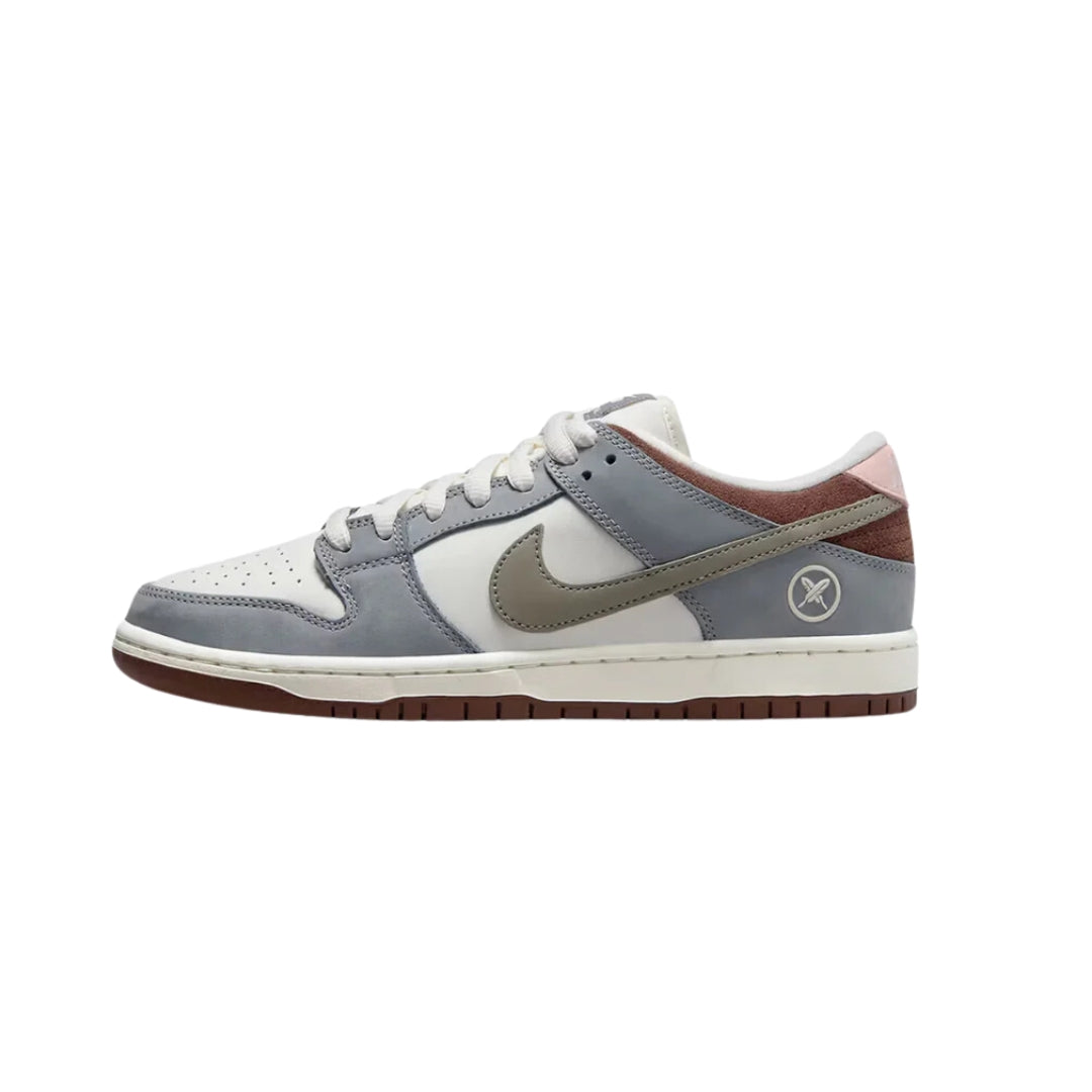 Nike SB Dunk Low Yuto Horigome features a white leather base with grey nubuck leather overlays, while Chocolate Brown suede panels appear on the collar and pink leather is seen on the heel tab with 'Nike' branding.