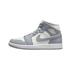  Nike Air Jordan 1 Mid "Stealth" (Women’s) sneakers featuring a sleek combination of light grey and white leather with subtle black accents. The mid-top design showcases the iconic silhouette, including a white midsole and a black swoosh, displayed against a neutral background to emphasize the shoe's modern and stylish appeal.



